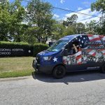 The Caravan for Disability Freedom and Justice. A woman sits in the driver's seat with her arms crossed in an X with the East Central Regional Hospital - Gracewood entry sign in back.